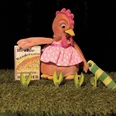 seifenblasen-theater-henriette-und-die-wunderkoerner.jpg Handpuppe Henne in rosa Kleid mit grünem Wurm auf Bühnenwiese, Kulisse aus Gras und Pflanzen