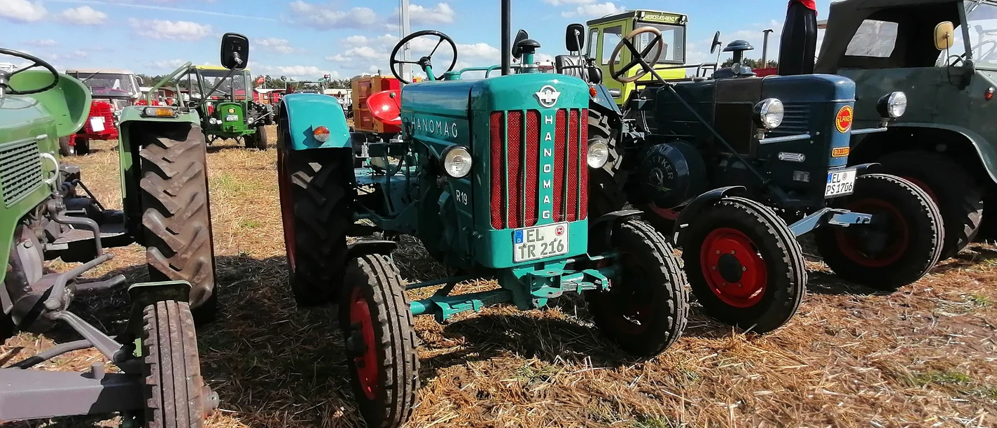 Trecker von Hanomag und Lanz gehörten zu den frühesten im Emsland. ©H. H. Bechtluft – Fotos Repro.jpg Alte Hanomag- und Lanz-Traktoren stehen nebeneinander auf einem Feld bei sonnigem Wetter.