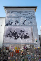 Ein großes Wandbild zeigt eine historische Fotografie von 13 Personen. Das Gebäude ist urban gestaltet mit verschiedenen Streetart-Elementen.