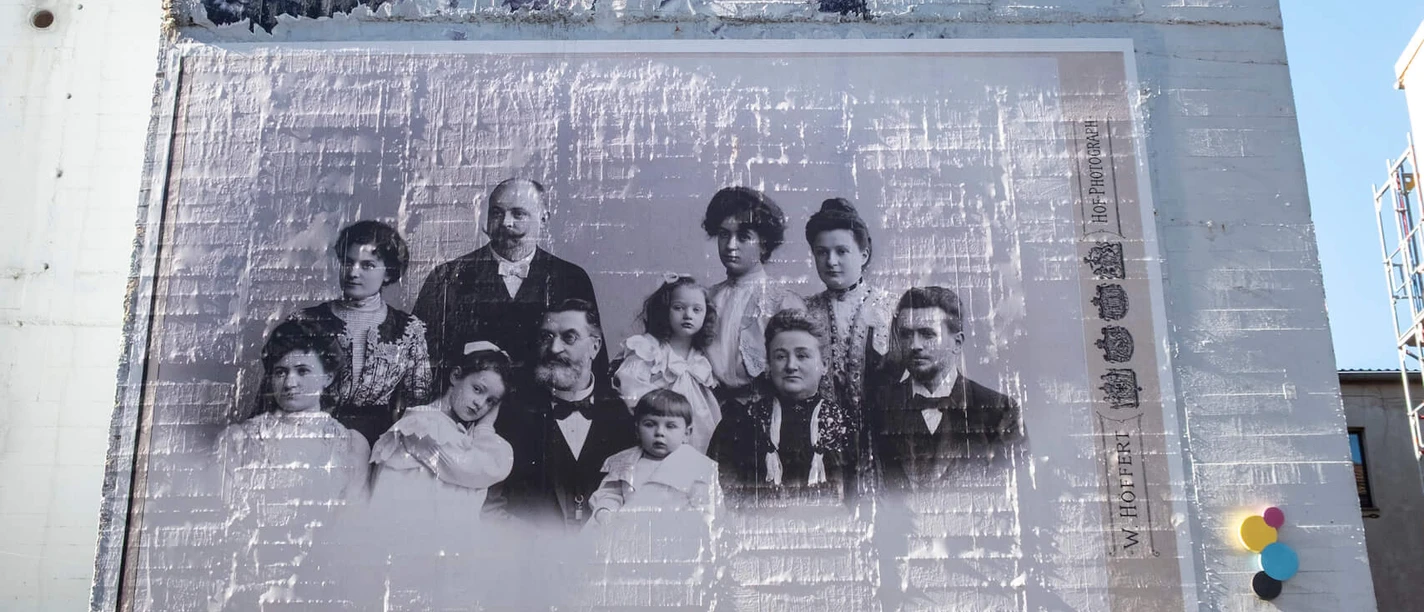 A large mural shows a historical photograph of 13 people. The building has an urban design with various street art elements.