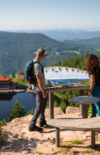 Zwei Wanderer am AugenBlick mit Aussicht auf den Mummelsee und ins Tal