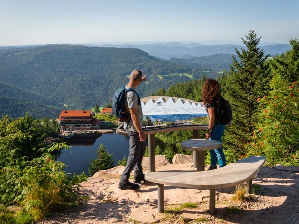 Zwei Wanderer am AugenBlick mit Aussicht auf den Mummelsee und ins Tal