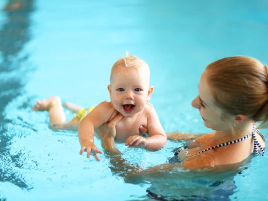 Baby u. Kleinkinderschwimmen im Koppke Greetsiel Ein lachendes Baby im Wasser im Arm der Mutter.