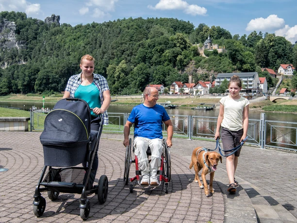 Barrièrevrij geluidsterras Een vrouw met een kinderwagen, een rolstoelgebruiker en een kind met een aangelijnde hond lopen en rollen over het geluidsterras.
