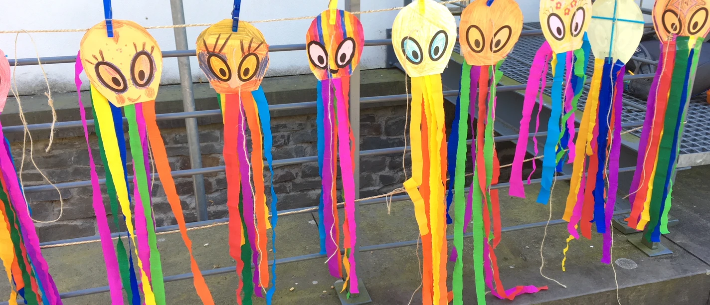 Drachenbau Bunte selbst gebastelte Drachen mit langen Papierstreifen hängen an einer Leine.