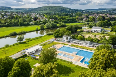 Luftaufnahme des Freibads Höxter im Grünen, umgeben von Bäumen und nahe am Fluss gelegen.