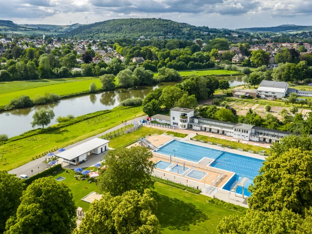 Luftaufnahme des Freibads Höxter im Grünen, umgeben von Bäumen und nahe am Fluss gelegen.