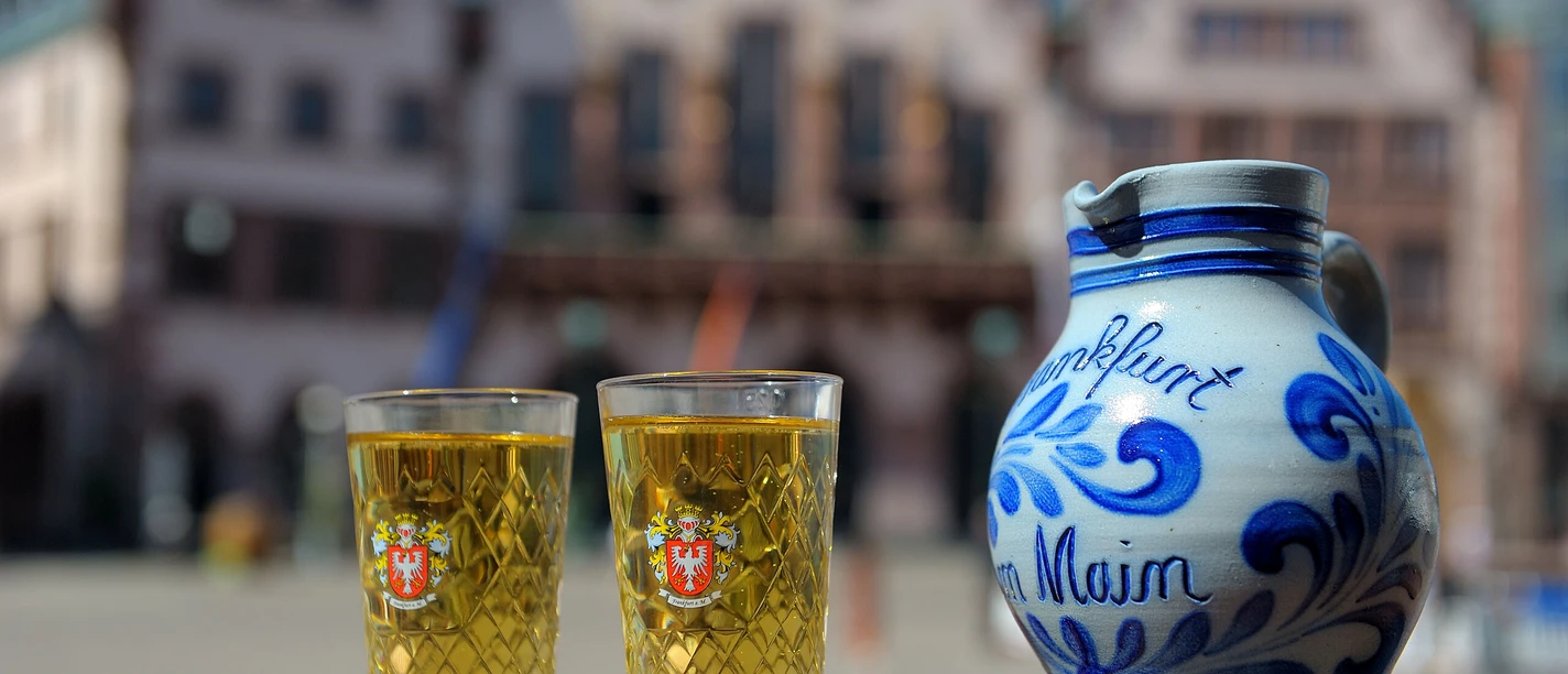 Apfelwein für Einsteiger Traditioneller Bembel mit Apfelwein-Gläsern vor Frankfurter Altstadt.
