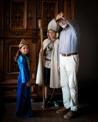 Online-Schloss-Kinderfuehrung-13.jpg Kinderen in middeleeuwse kostuums en een oudere man met een hoed in een historische kamer.