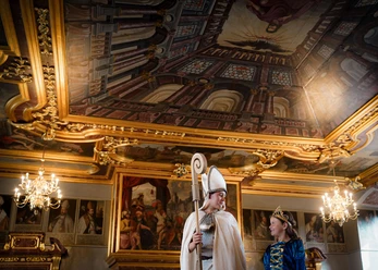 Online-Schloss-Kinderfuehrung-22.jpg Bishop and princess in medieval costume in a gilded baroque room under a magnificent ceiling.