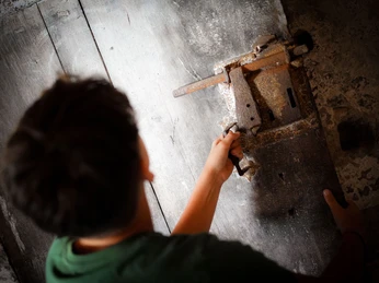 Online-Schloss-Kinderfuehrung-32.jpg Mensch dreht rustikalen Metallhebel an einer Holztür von oben gesehen.