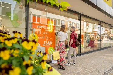 Zwei Personen betrachten ein Schaufenster mit sonnigem Motiv in einer Einkaufsstraße in Höxter.