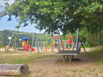 Spielplatz am Lütauer See - Badestelle Campingplatz.jpeg Spielplatz mit Klettergerüst und Rutsche am Lütauer See, umgeben von Bäumen.