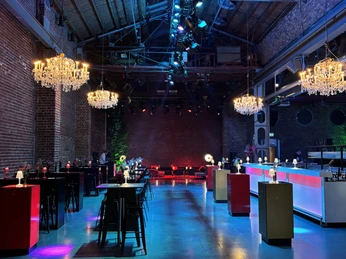 BALLONI Halle_11 Halle mit hohen Decken, Backsteinwänden, Kronleuchtern und bunter Beleuchtung für Veranstaltungen.Hall with high ceilings, brick walls, chandeliers and colorful lighting for events.
