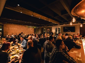 Ein voller Gastraum im Bürgerhaus Ratingen Der Gastraum im Bürgerhaus Ratingen ist gefüllt mit geselligen Menschen an Holztischen.