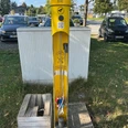 Radservice-Station Das Bild zeigt eine gelbe Radservice-Station mit Werkzeugen, umgeben von geparkten Autos und Bäumen.