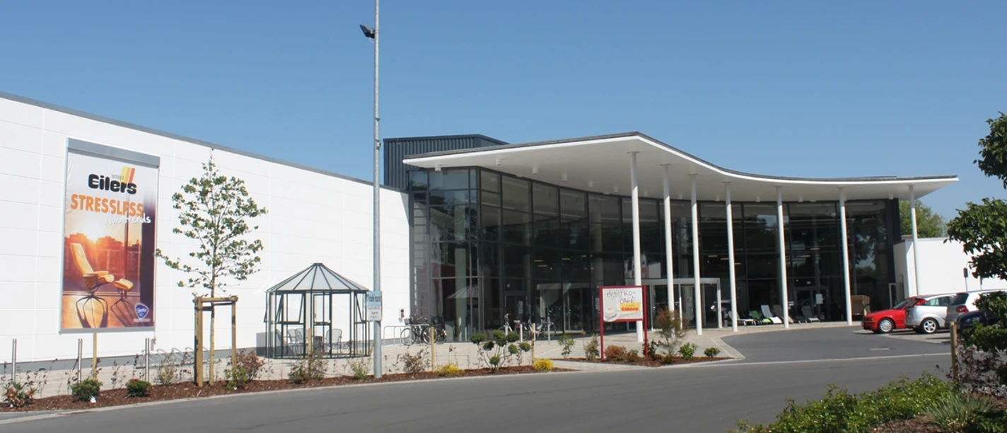 Möbel Eilers Eingangsbereich eines grossen Möbelhauses mit Sitzgelegenheit. Rechts ist ein Teil des Parkplatzes zu sehen.