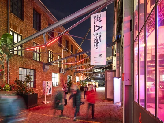 MACHWERKHAUS Belebtes Kunstzentrum bei Nacht mit roten Backsteinwänden, Menschen treten durch Eingang.Lively art center at night with red brick walls, people enter through the entrance.
