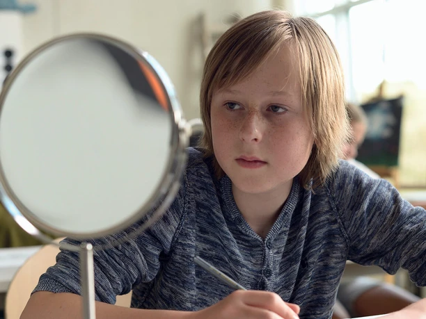 Filmstill zu "Ab morgen bin ich mutig" Junge sitzt in einem Raum mit Spiegel und schreibt konzentriert.
