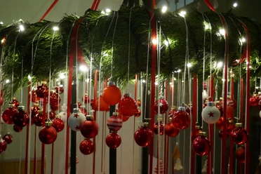 Leuchtender Weihnachtskranz mit roten Kugeln und Bändern, umringt von warmen Lichterketten.