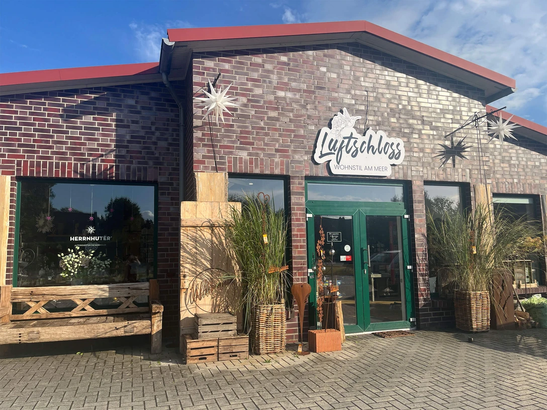 Luftschloss-Wohnstil-am-Meer.jpg Backsteingebäude mit grünem Vordach, dekoriert, mit Pflanzen und Sternen, Eingangstür aus Glas.