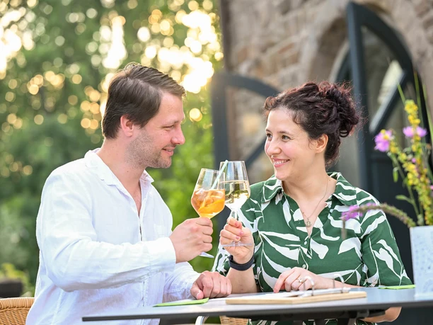 Café Ruhrnatur, Mülheim an der Ruhr Ein Paar hebt die Gläser in einem Café bei sommerlichem Abendlicht, umgeben von Natur.