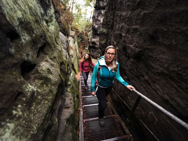 Aufstieg zum Papststein Zwei Frauen steigen eine Metalltreppe in einer engen Felsenschlucht hinauf.