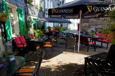 Biergarten, Dingle`s Irish Pub in Mettmann Ein Biergarten mit dunklen Holztischen und roten Sitzauflagen unter Guinness-Sonnenschirmen.