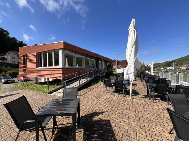 Restaurant met modern, rood gelambriseerd gebouw, grote ramen aan de voorkant en terras op de begane grond