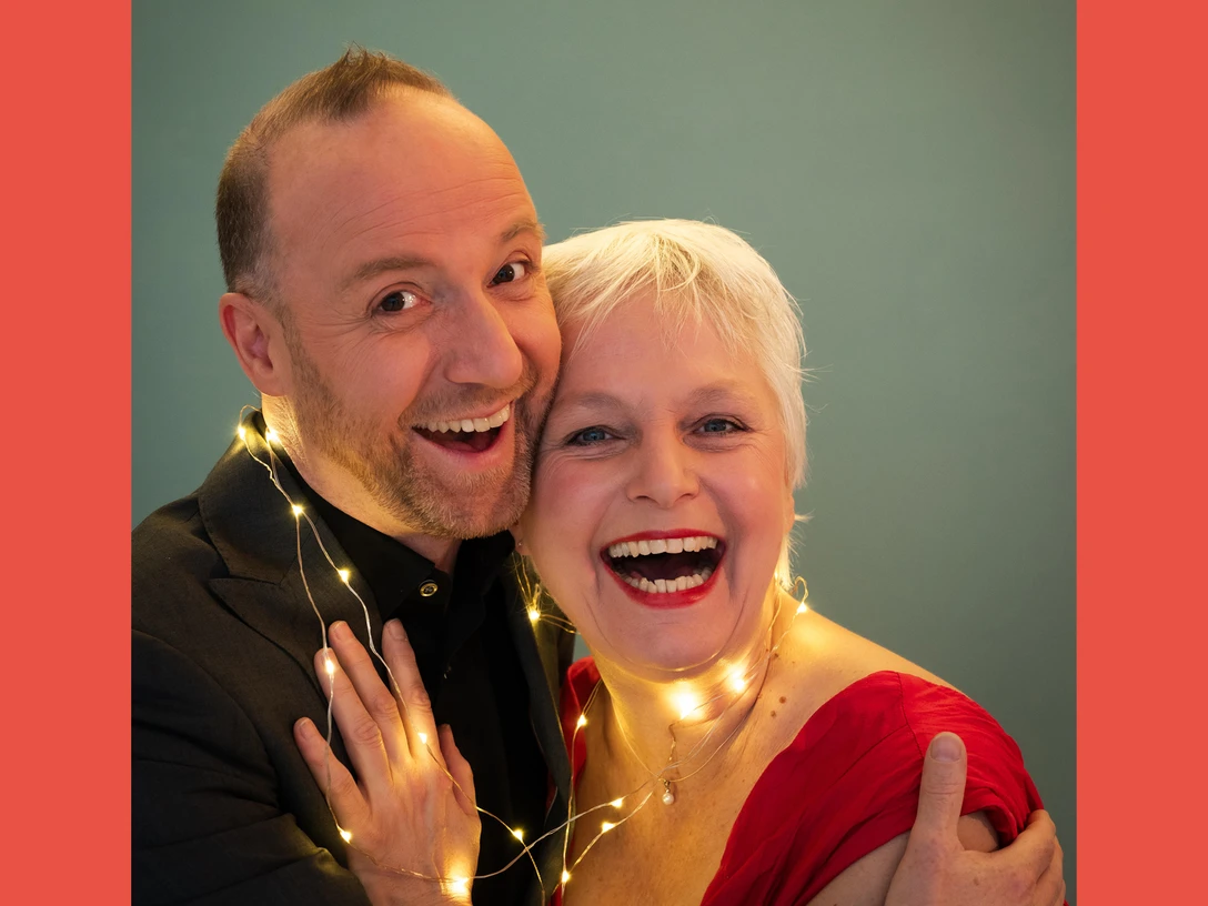 251216_Lametta.jpg Ein fröhliches Paar mittleren Alters lächelt, umgeben von einer Lichterkette vor grünem Hintergrund.A cheerful middle-aged couple smiles, surrounded by a string of lights against a green background.Veselý pár středního věku se usmívá, obklopen světelným řetězem na zeleném pozadí.Wesoła para w średnim wieku uśmiecha się, otoczona sznurem świateł na zielonym tle.Een vrolijk koppel van middelbare leeftijd lacht, omringd door een koord van lichtjes tegen een groene achtergrond.Un'allegra coppia di mezza età sorride, circondata da un filo di luci su uno sfondo verde.