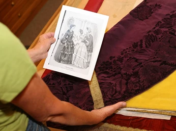 Ein dunkler Stoff liegt auf einem Tisch, daneben hält eine Hand eine schwarz-weiße Zeichnung fest.