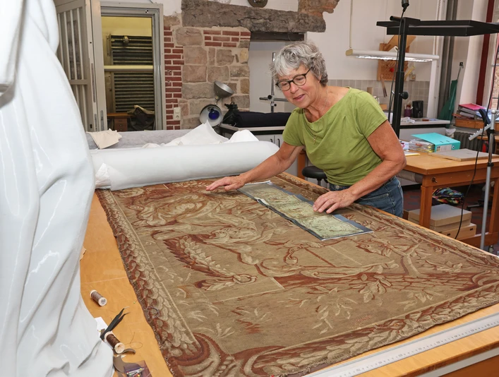 Eine Frau präsentiert ein kunstvoll bearbeitetes Gewebe auf einem Arbeitstisch.