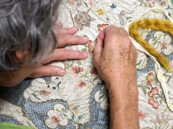 Eine Frau arbeitet konzentriert an einem farbenfrohen Handarbeitsstück.