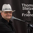 251223_StelzerFriends.jpg Thomas Stelzer, mit Hut und Brille, sitzt am Klaviermikrofon vor einem dunklen Hintergrund.Thomas Stelzer, wearing a hat and glasses, sits at the piano microphone in front of a dark background.Thomas Stelzer v klobouku a brýlích sedí u mikrofonu klavíru na tmavém pozadí.Thomas Stelzer, w kapeluszu i okularach, siedzi przy mikrofonie fortepianu na ciemnym tle.Thomas Stelzer, met hoed en bril, zit aan de pianomicrofoon voor een donkere achtergrond.Thomas Stelzer, con cappello e occhiali, siede al microfono del pianoforte davanti a uno sfondo scuro.