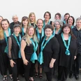 251224_StGospel.jpg Eine Gruppe von 19 Sängern in schwarz und türkis schalbekleidet vor einer hellen Wand.A group of 19 singers dressed in black and turquoise shawls in front of a light-colored wall.Skupina 19 zpěvaček oblečených do černých a tyrkysových šátků před světlou stěnou.Grupa 19 śpiewaków ubranych w czarne i turkusowe szale przed jasną ścianą.Een groep van 19 zangers gekleed in zwarte en turquoise sjaals voor een lichtgekleurde muur.Un gruppo di 19 cantanti vestiti con scialli neri e turchesi davanti a una parete chiara.