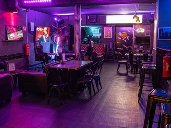 Gaming Area Lost Level Eine Gaming-Lounge mit dunklem Ambiente, ausgestattet mit Spielstationen und Barhockern.A gaming lounge with a dark ambience, equipped with gaming stations and bar stools.