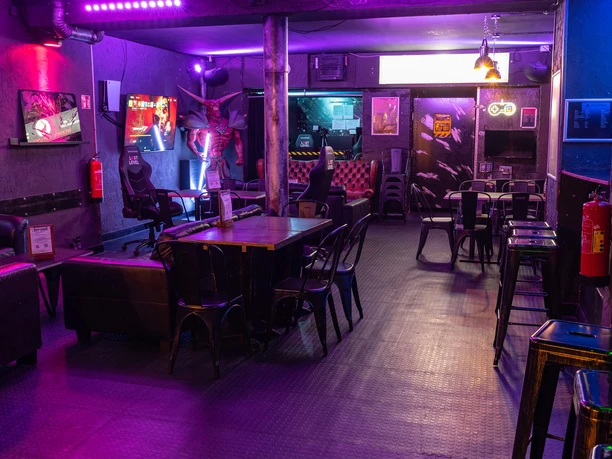 Gaming Area Lost Level Eine Gaming-Lounge mit dunklem Ambiente, ausgestattet mit Spielstationen und Barhockern.