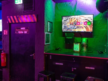 Gaming Area PS4 & XBOX A gaming zone with PS4 and Xbox consoles, gloomily lit, with bar stools in front of display screens.