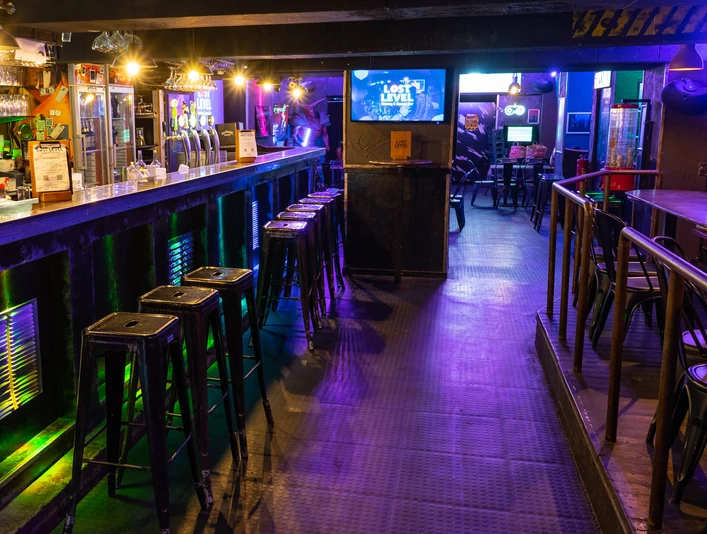 Lost Level bar area Langgestreckter Barbereich mit Barhockern in gedämpftem Licht. Fernseher an den Wänden.Elongated bar area with bar stools in subdued lighting. Televisions on the walls.