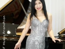 Porträt einer lächelnden Musikerin in einem silbernen Kleid vor einem Flügel, elegant posierend.