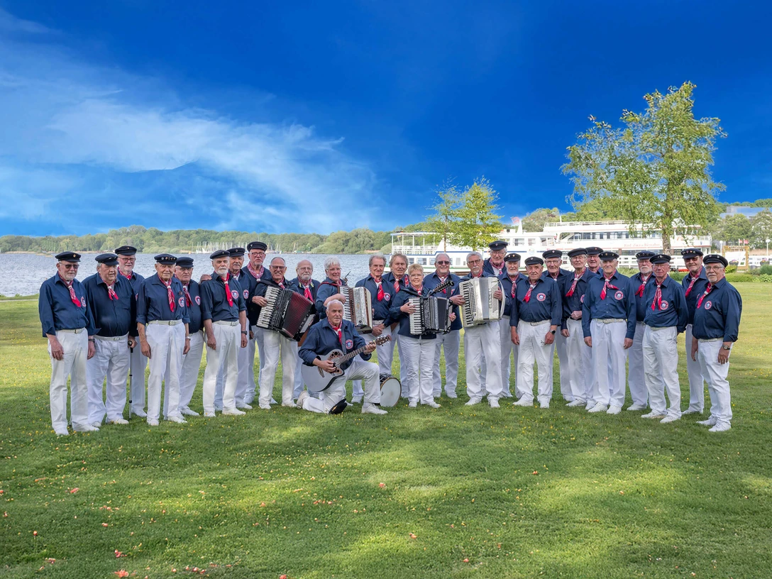 Shanty-Chor-Bad-Zwischenahn.jpg Shanty-Chor Bad Zwischenahn in maritimen Outfits, posierend auf einer Wiese im Kurpark vor dem Zwischenahner Meer vor blauem Himmel.