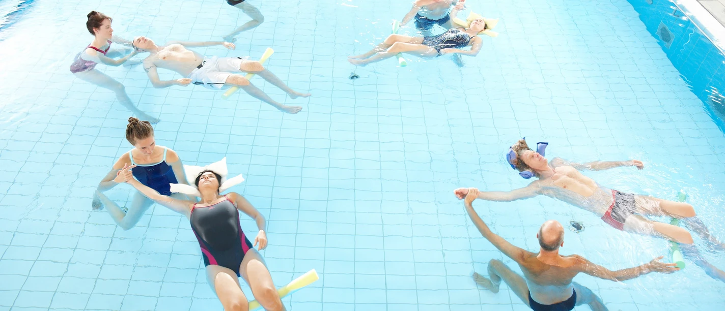 AR Gruppe von oben Gruppe entspannt im warmen Wasserbecken, Teilnehmer treiben ruhig bei einem AquaRelax-Kurs.