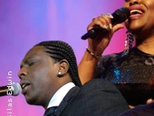 Zwei Sängerinnen und Sänger mit Mikrofonen auf einer Bühne in leidenschaftlichem Gesang.