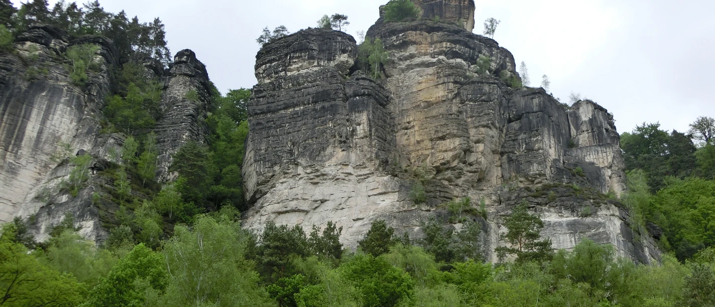 Massive Sandsteinfelsen erheben sich aus grüner Vegetation vor einem bewölkten Himmel.