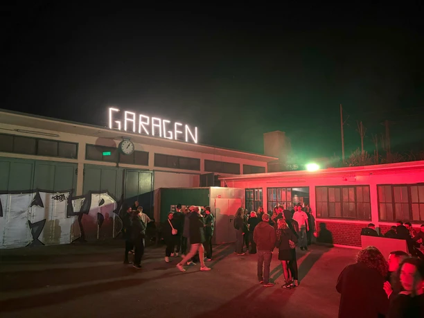 Garagen Club Menschen versammeln sich nachts vor einem beleuchteten Gebäude mit dem Schriftzug "GARAGEN".