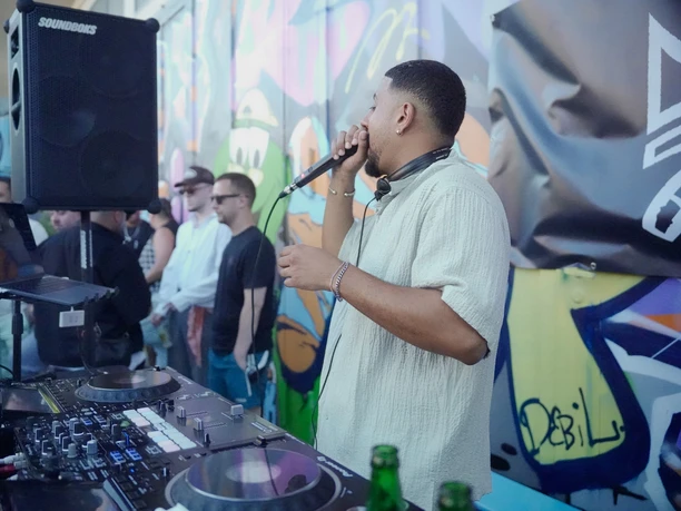 Garagen Club A DJ stands in front of a colorful graffiti wall and mixes music in front of an audience.