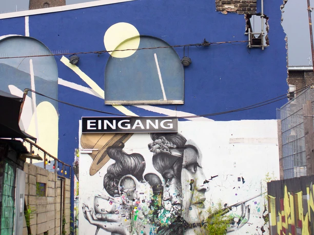 Helios37 Außenbereich Ein farbenfrohes Wandgemälde zeigt drei Menschen in Comic-Stil unter einem bogenförmigen Fenster.