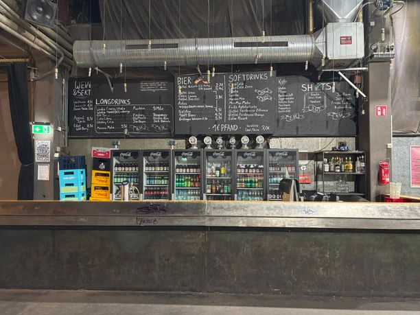 Live Music Hall A bar with a chalkboard menu, fridges full of drinks and an industrial ceiling design.