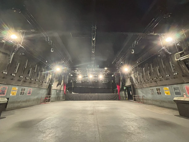 Live Music Hall Die leere Halle mit Bühne der Live Music Hall mit dunkler Decke und hellem Boden, von hellen Scheinwerfern beleuchtet.