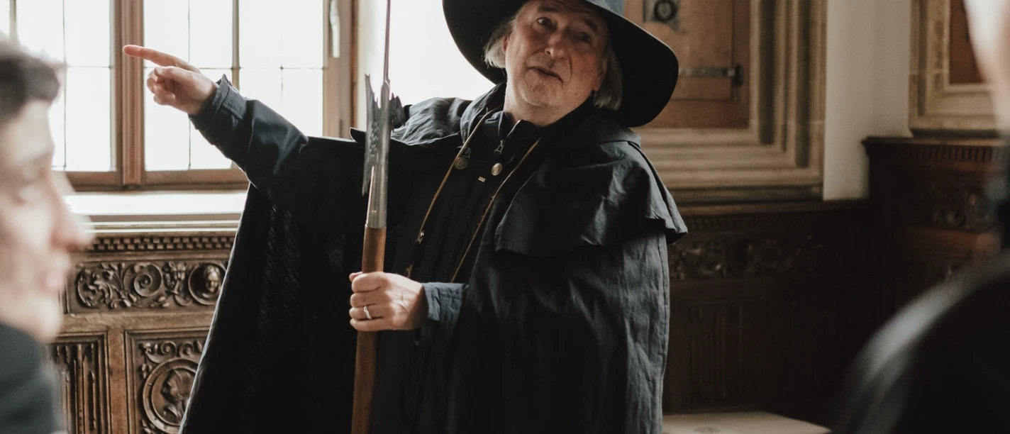 Nachtwächter (Hauptbild).jpg En nattevagt i historisk kostume forklarer detaljer for de besøgende i et traditionelt indrettet rum.